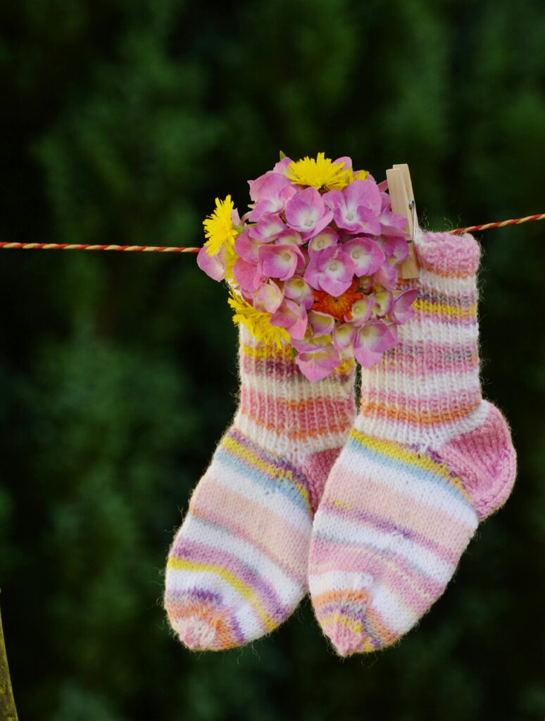 Striped wool socks hanging with flowers on a clothesline outdoors.