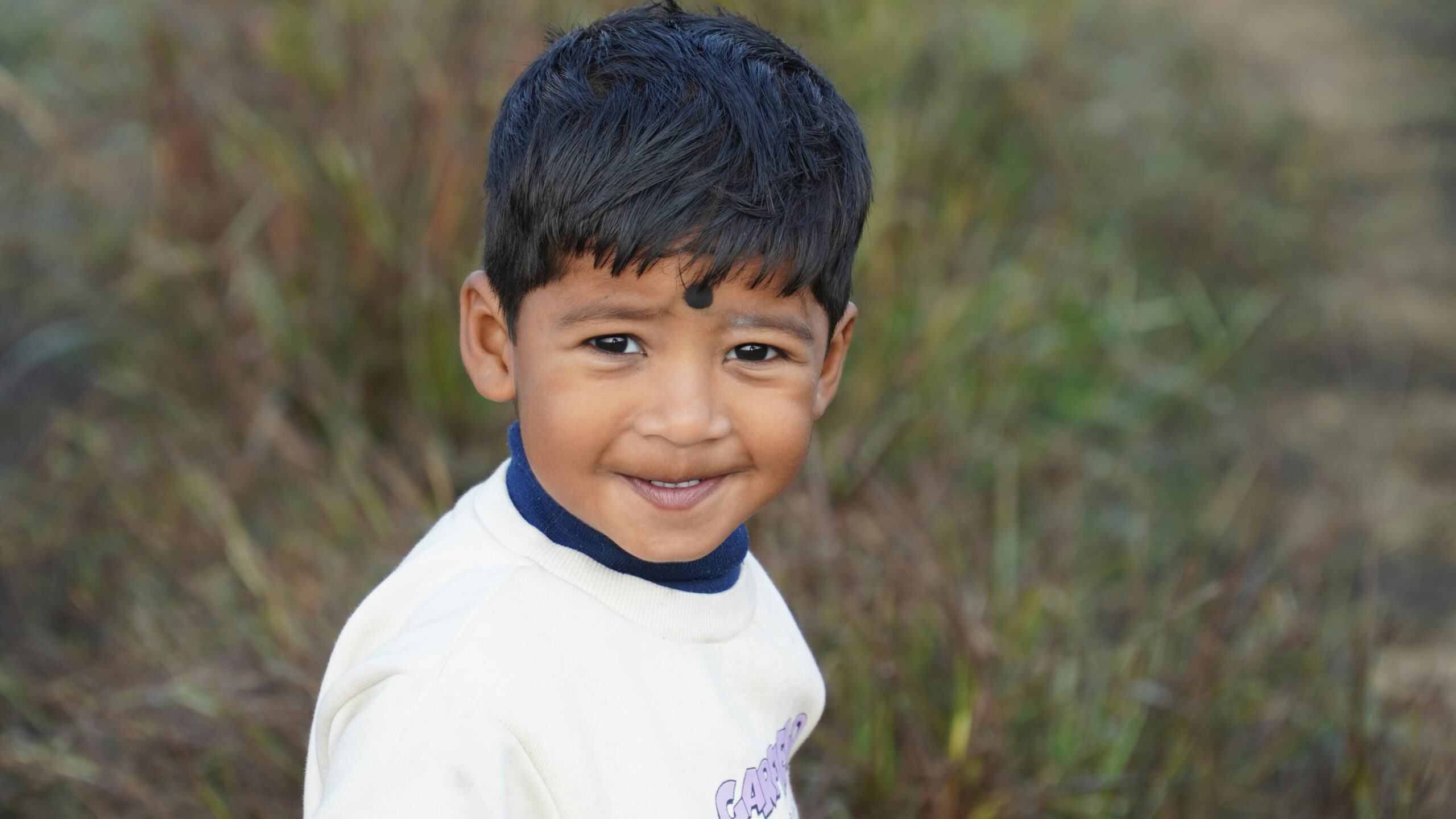 A cheerful South Asian boy outdoors in Jamshedpur, India, wearing a white shirt.